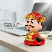 Solar-powered Caishen desk figurine nodding next to laptop in office setting